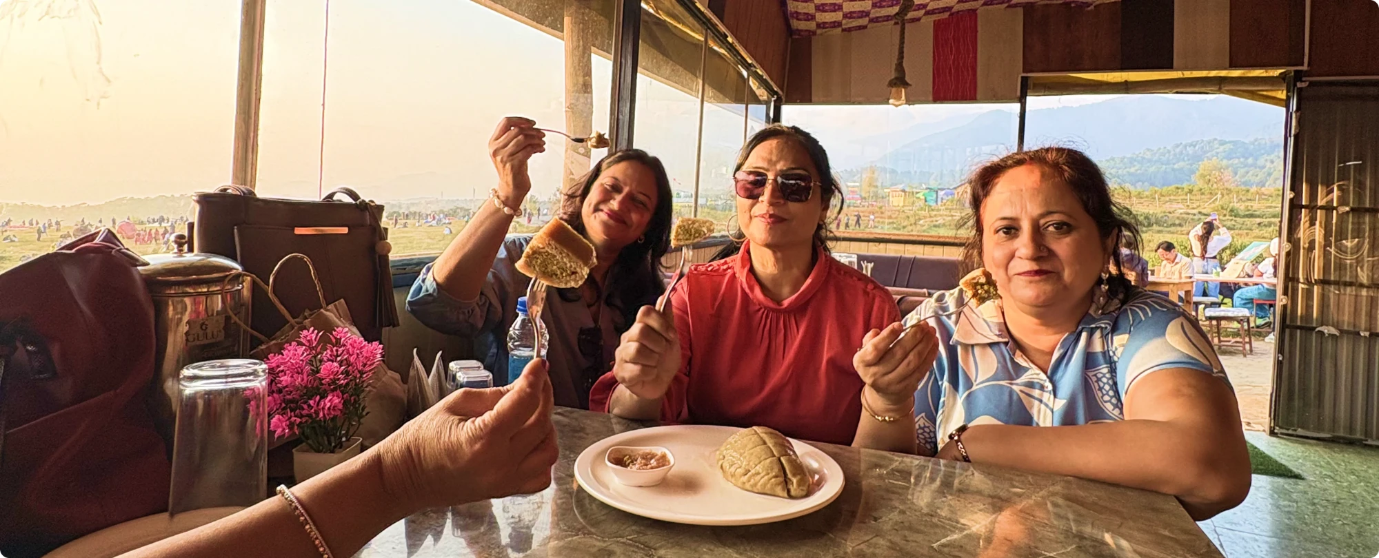 Three Sahelis holding up forkfuls of cake at a mountain café